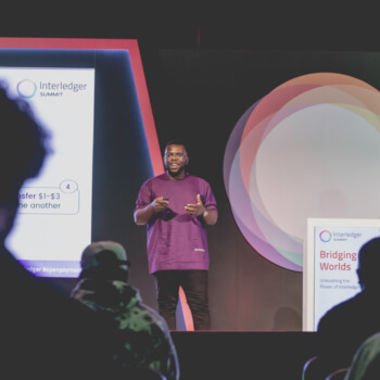 Uchi Uchebeke presenting on stage at Interledger Summit, with audience silhouettes in the foreground.